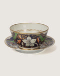 Front studio view of an antique British Imari style porcelain finger bowl sitting on its matching wide underplate, showing white flower blooms and gold detailing.