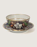 Front studio view of an antique British Imari style porcelain finger bowl sitting on its matching wide underplate, showing white flower blooms and gold detailing.