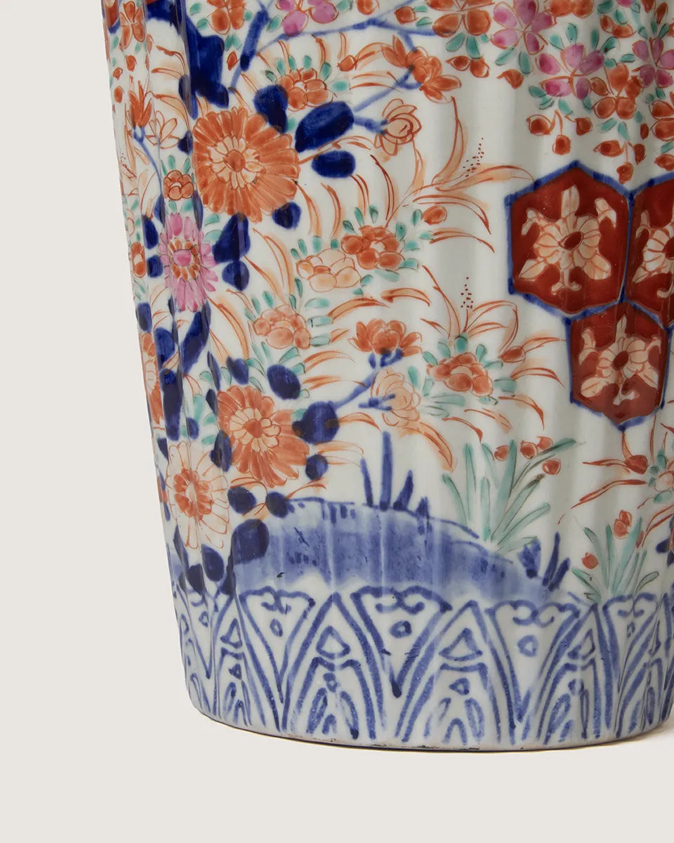 Close-up detailed view of the lower section of an antique Imari style fluted porcelain vase, showing hand-painted orange chrysanthemums, green leaves, and a geometric repeating border at the base.
