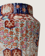 Close-up detailed view of the upper shoulder of an antique Imari style porcelain vase, showcasing vertical fluting and hand-painted patterns of traditional figures, phoenixes, and orange flowers.