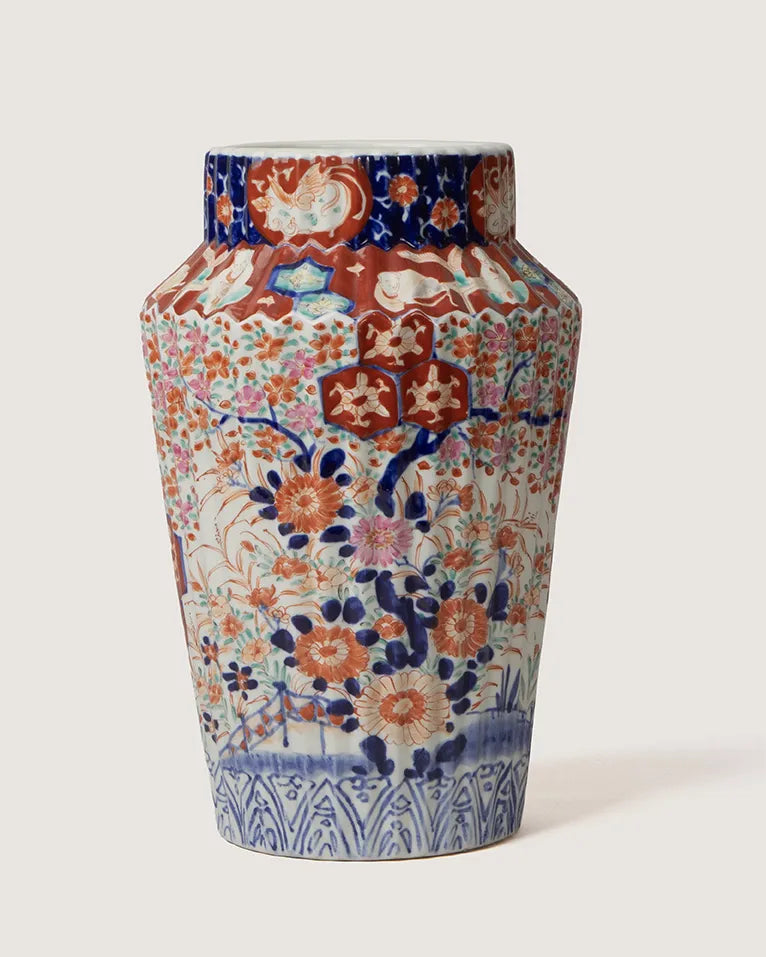 Full front view of an antique Imari style porcelain vase with a vertically ribbed body, hand-painted with a maximalist design of dense orange and pink chrysanthemums, phoenixes, and cobalt blue foliage.