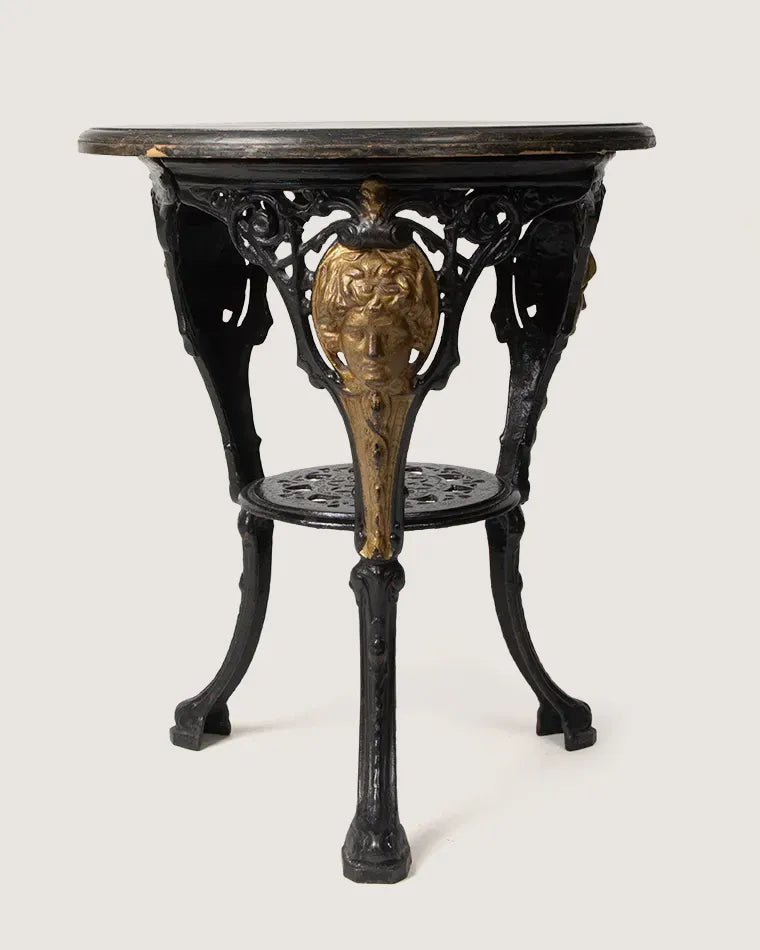 Late 19th-century Victorian bistro table featuring a heavy ornate cast iron base with gilded masks and a solid wood top.