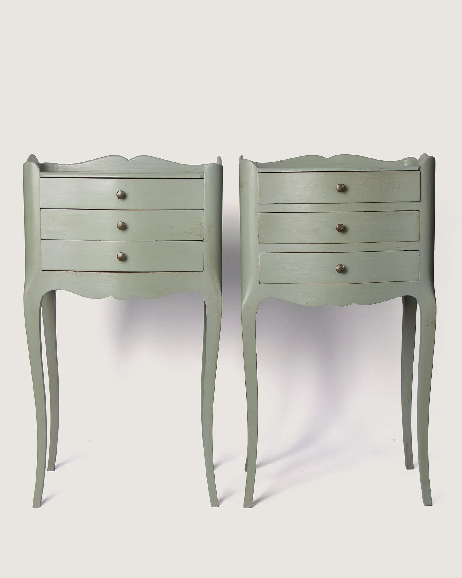 Full front view of the two unique antique French nightstands showing the symmetrical three-drawer design and slightly asymmetric undulating lines.