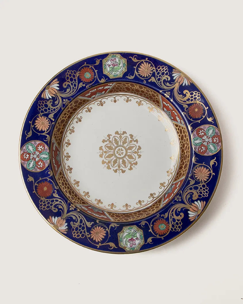 Full top-down view of an antique English Imari pattern deep plate, showcasing the rich cobalt blue border, gold floral scrolls, and central gold rosette.